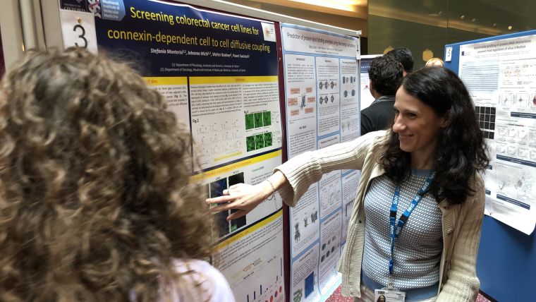 Stefania Monterisi shows a researcher her poster entitled "Screening colorectal cancer cell lines for connexin-dependent cell to cell diffusive coupling"