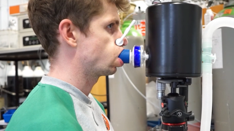 A male individual breathes into a scientific sensor device.