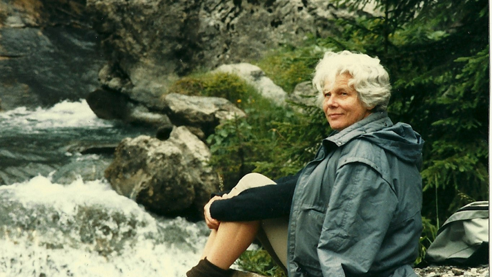 Marianne sat by a river in a raincoat