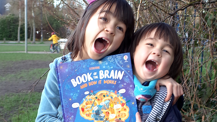 Betina Ip's daughters pictured laughing and holding a copy of Book of the Brain in the park.