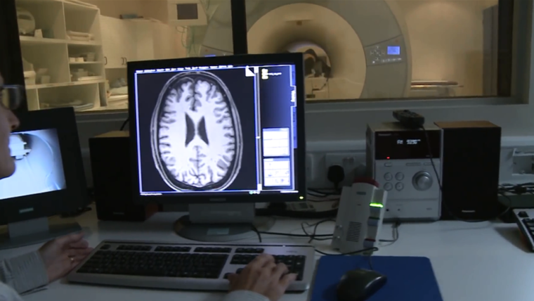 A researcher conducting an MRI - a brain scan displays on the computer screen with the machine in the background